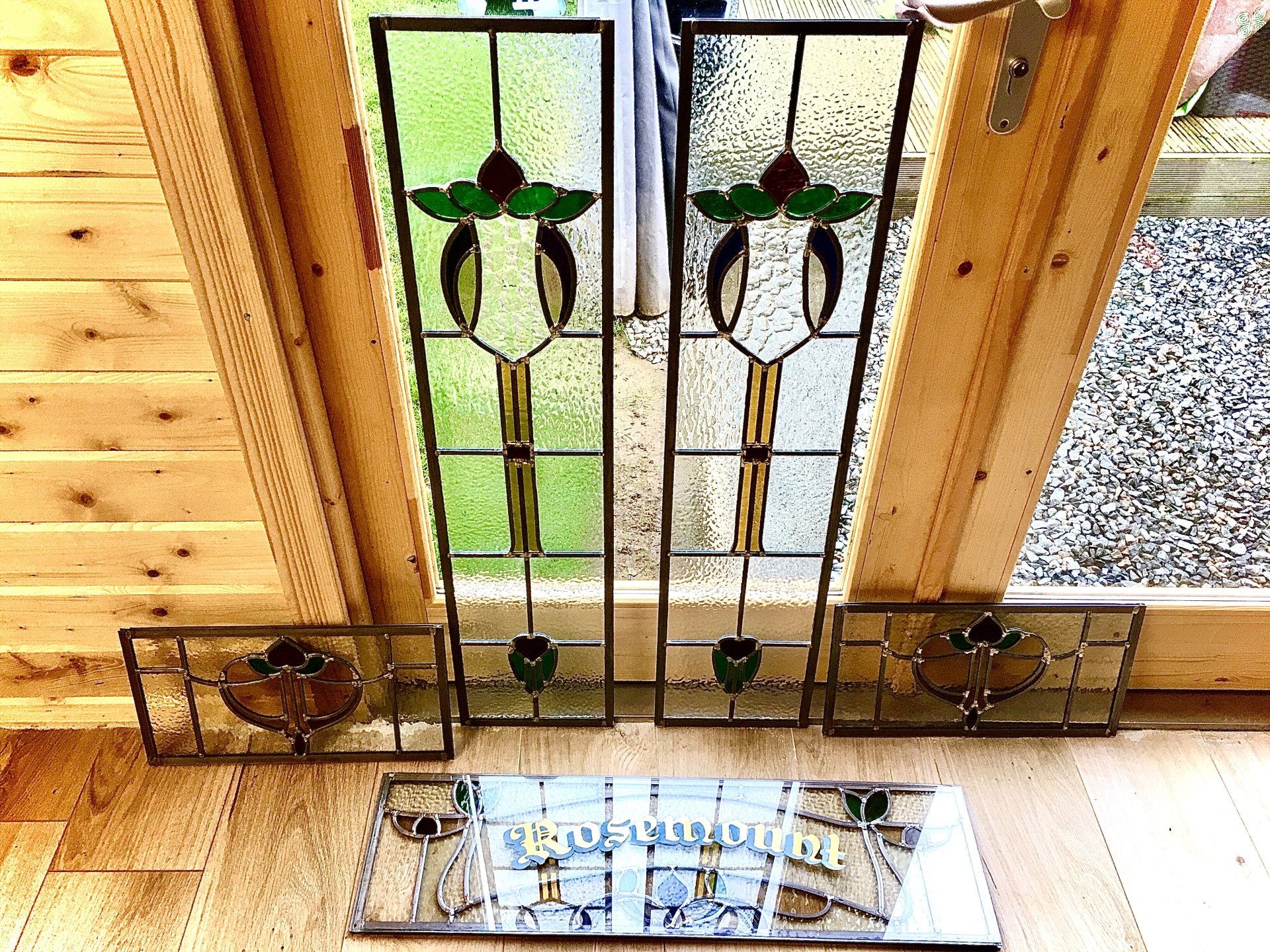 Stained-glass windows above a wooden floor, with decorative black metal trim and a small glass table below.