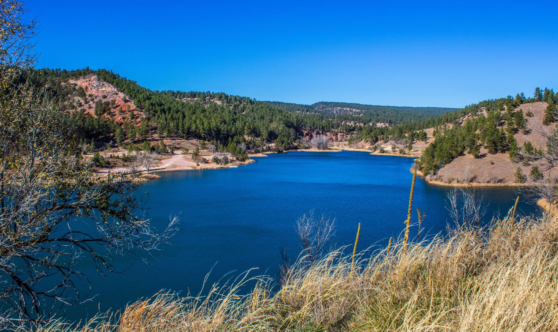 A large body of water surrounded by mountains and trees on a sunny day.