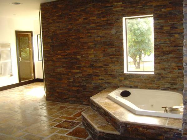 Bathroom with stone walls, tiled floor, jacuzzi tub, and window overlooking a tree.