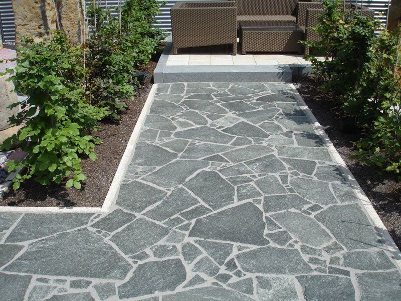Flagstone pathway leading to patio seating, flanked by green shrubs.