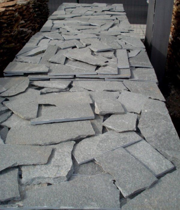 Pile of irregularly shaped gray stone tiles, possibly for paving.