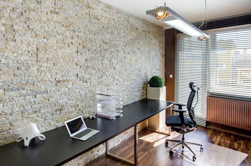 Modern office space with a stone wall, long black desk, laptop, and office chair.