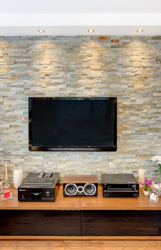 Flat-screen TV mounted on stone wall, above wooden entertainment unit with speakers and components.