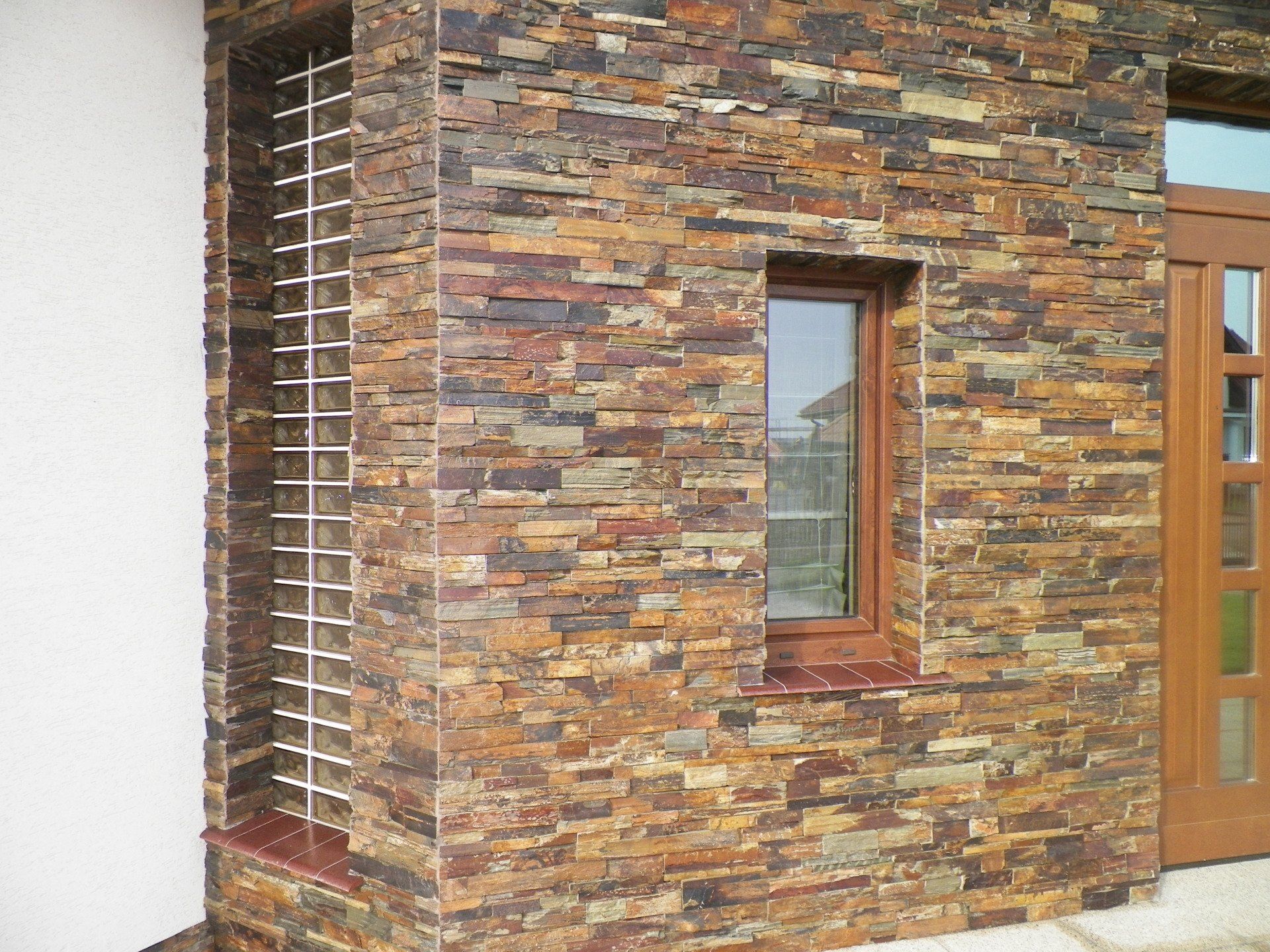 Corner of a building with stone veneer walls, small window, wooden door, and a decorative metal grate.