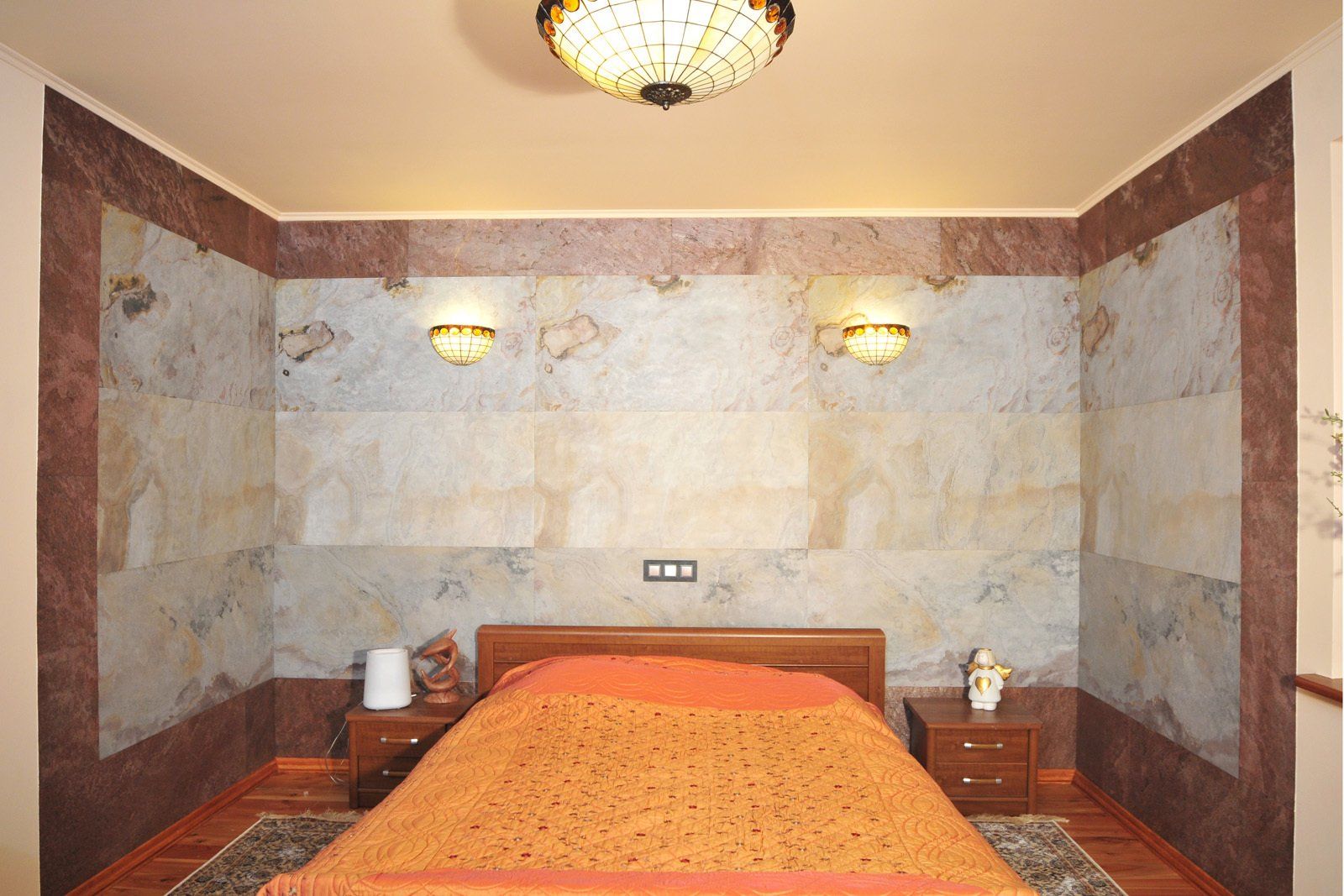 Bedroom with marble-like wall panels, brown bed, and sconce lighting.