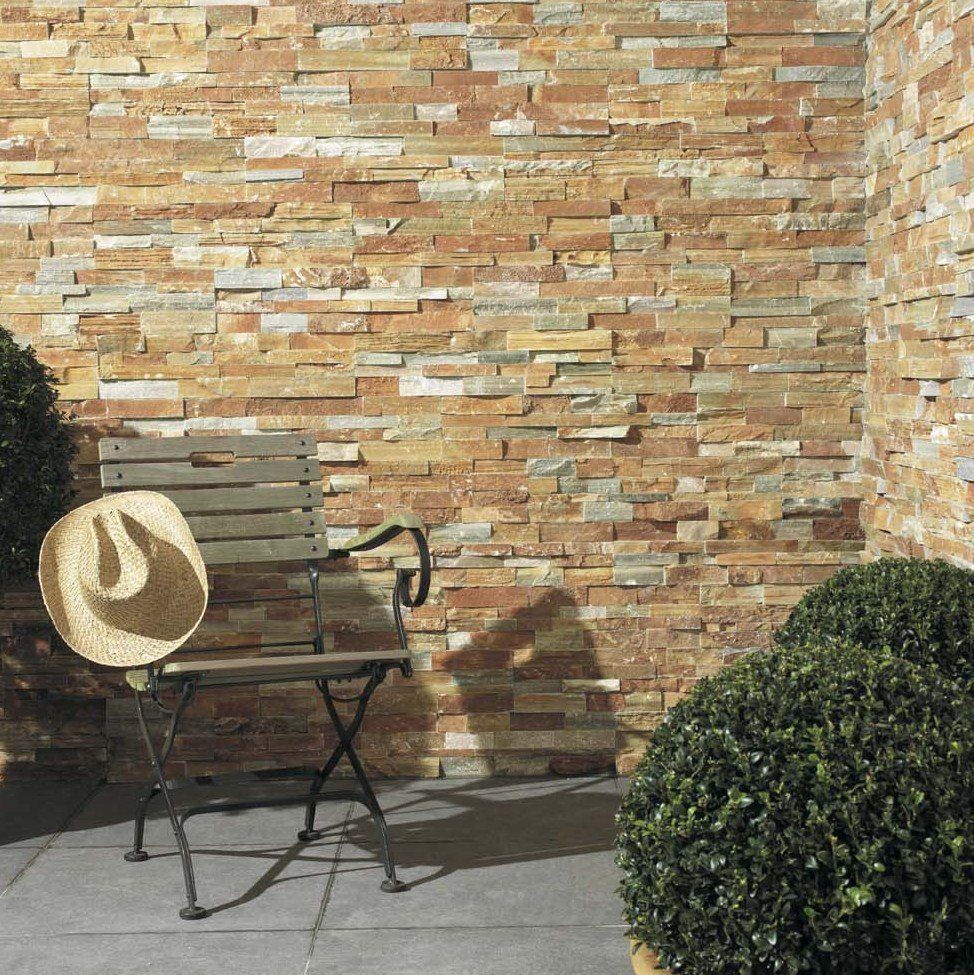 Chair with a hat beside a stone wall in an outdoor setting with shrubs.