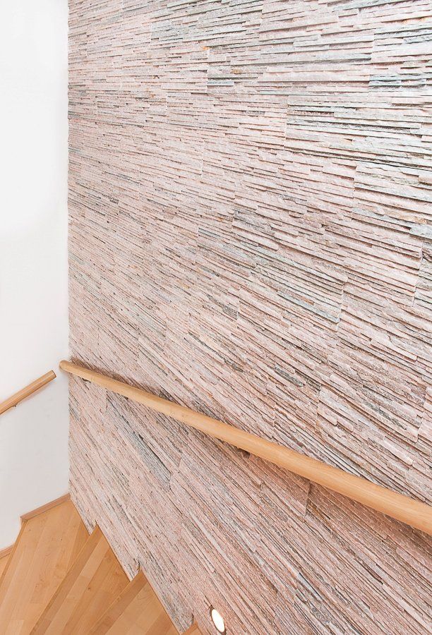 Wooden staircase with a handrail. Textured wall of horizontal, light and dark colored stone.