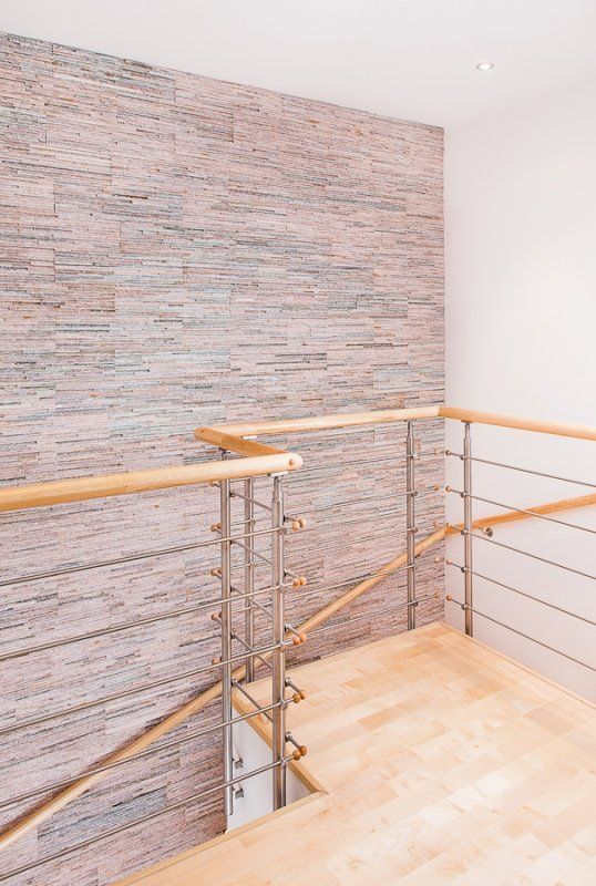 Interior view of a landing with wooden floors and a stone wall. Stainless steel and wooden railing.