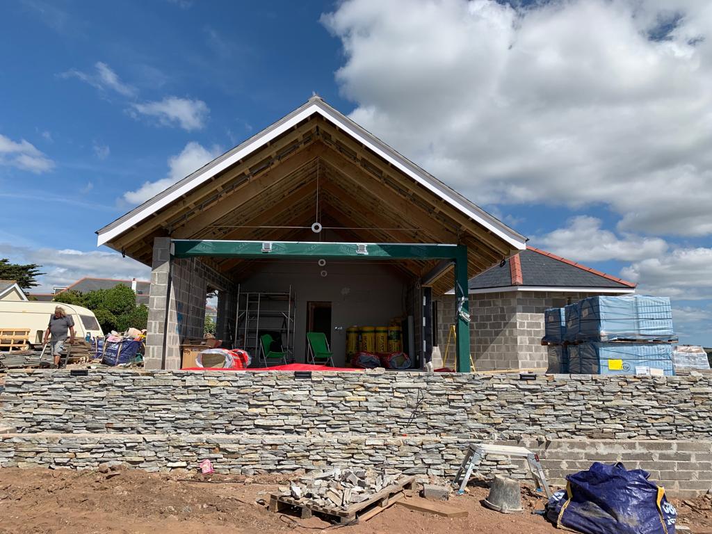 Construction site: partially built building with stone and wood structure, blue sky, and construction materials.