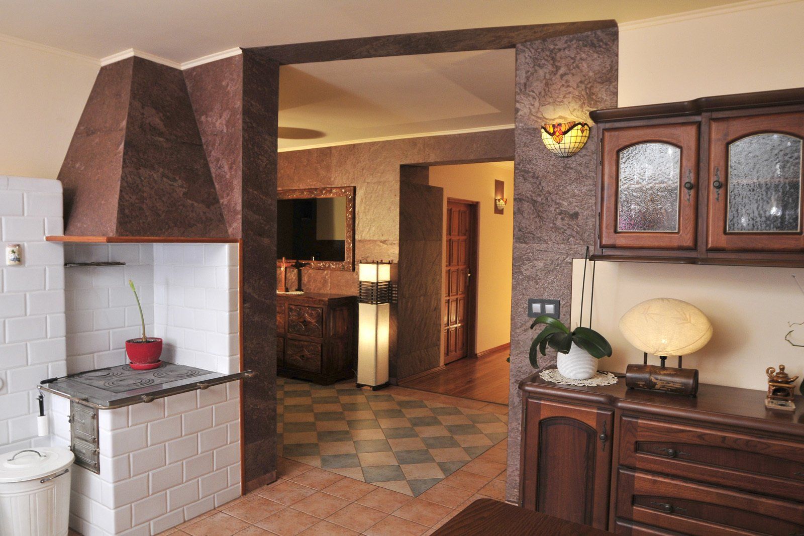 Interior view of a kitchen and hallway, featuring a brick fireplace, cabinets, and stone walls.