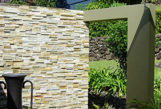 Stone wall with an archway opening onto a grassy area with plants and a stone wall backdrop.
