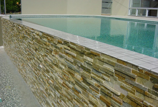 Swimming pool with a stone veneer wall. Water overflows into a lower area.