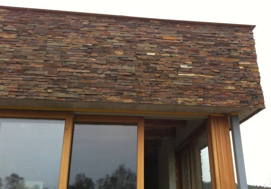 Stone facade over wooden-framed windows of a building. Brown, rectangular stones. Bright sky.