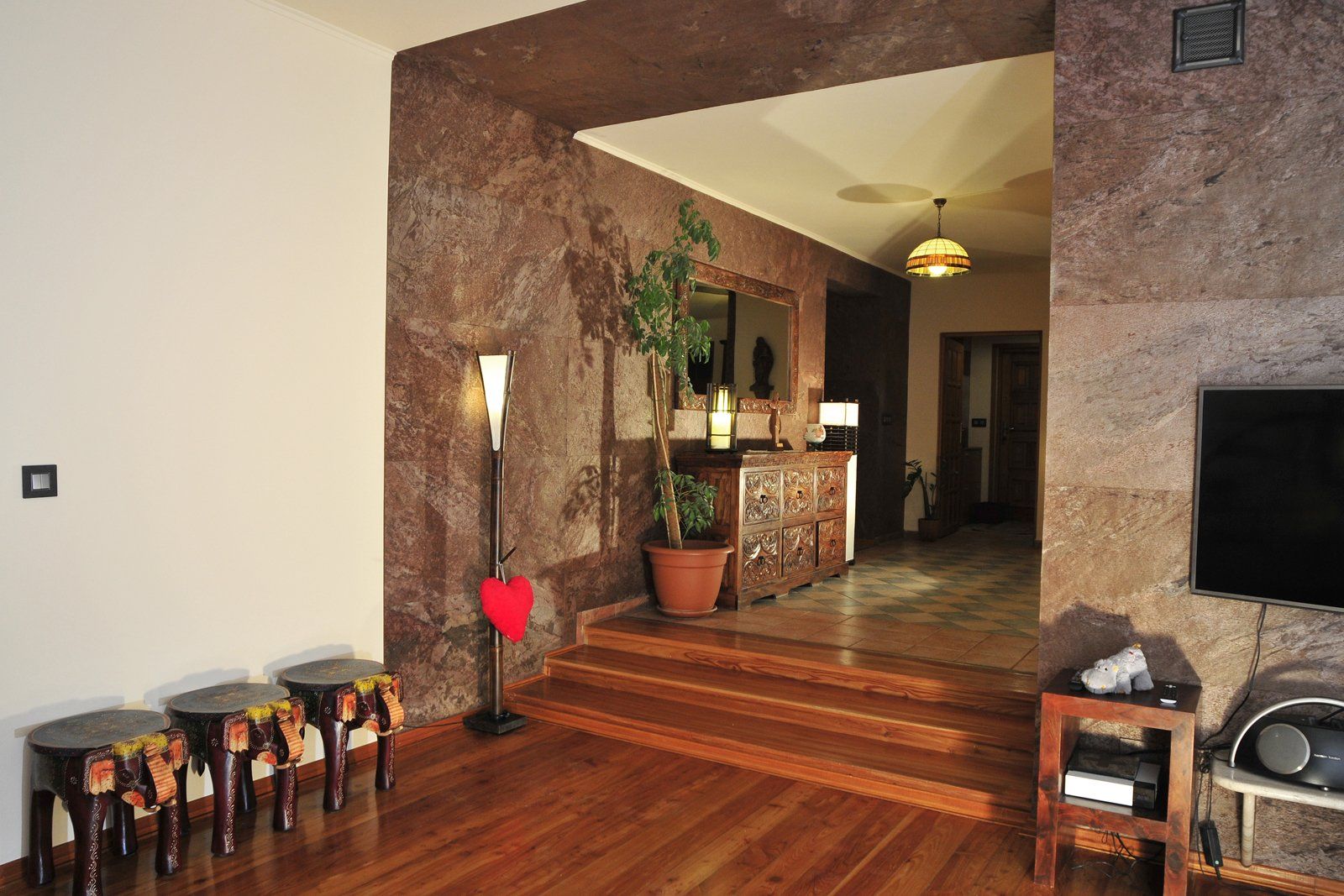 Entryway with stone walls, wooden floor, steps, and furnishings. A plant, art, and TV are visible.