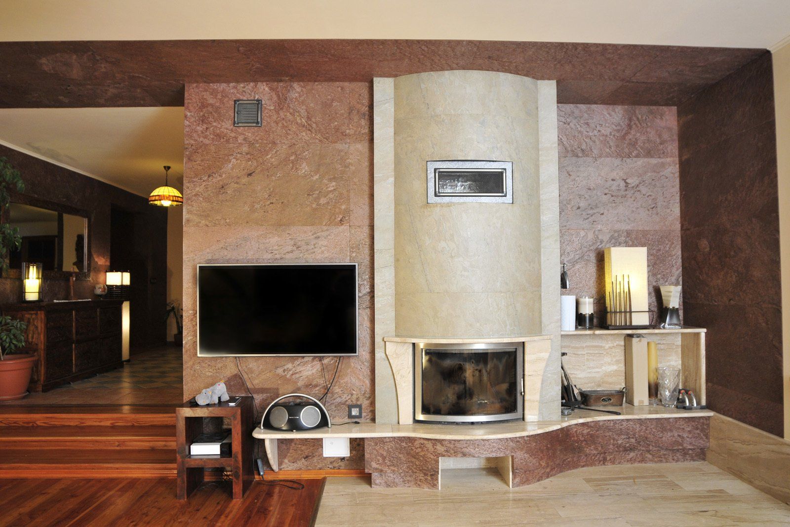 Living room with a stone fireplace, TV, and open doorway to another room with wooden floor.