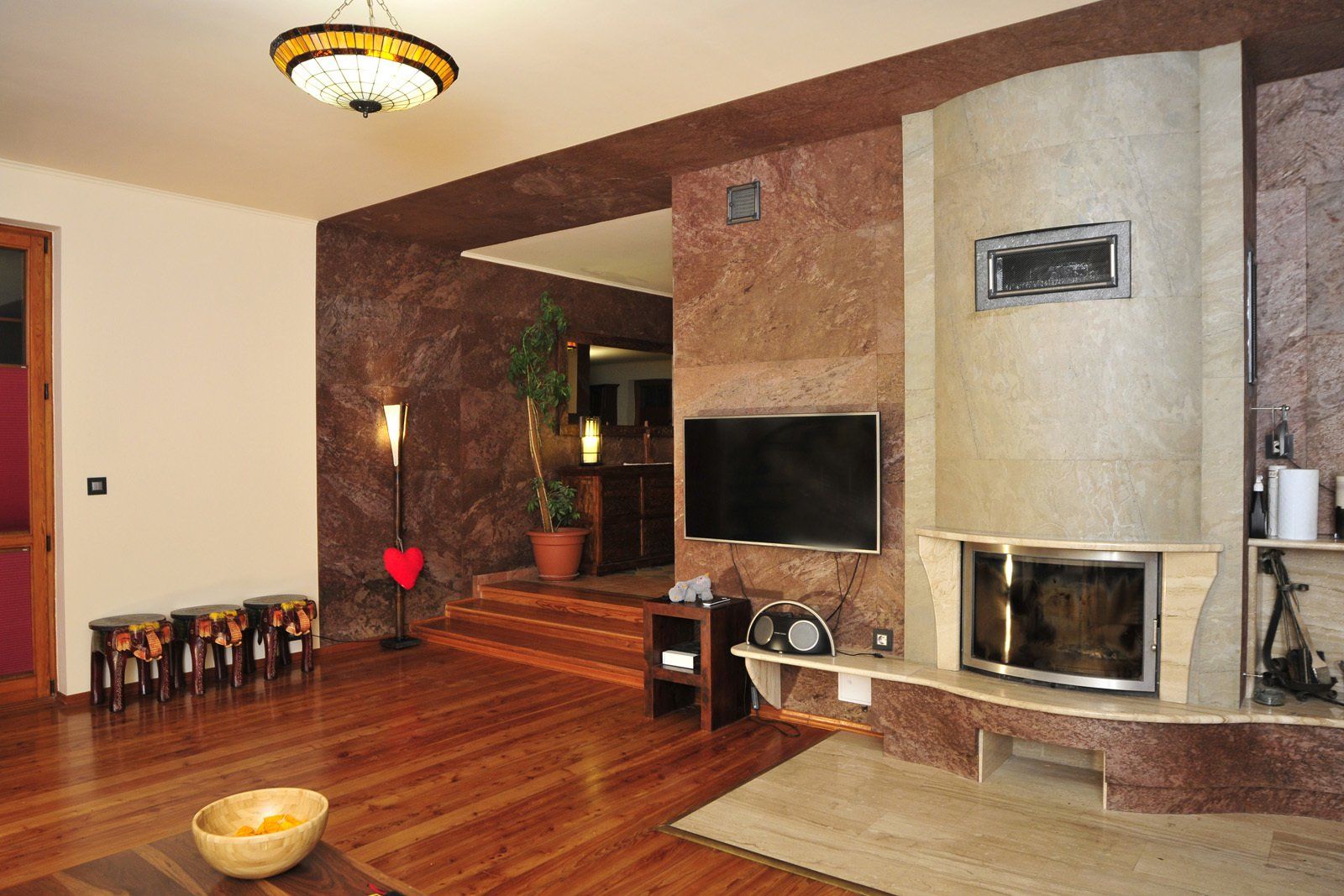 Living room with fireplace, TV, and wooden floor; brown and beige tones dominate the space.