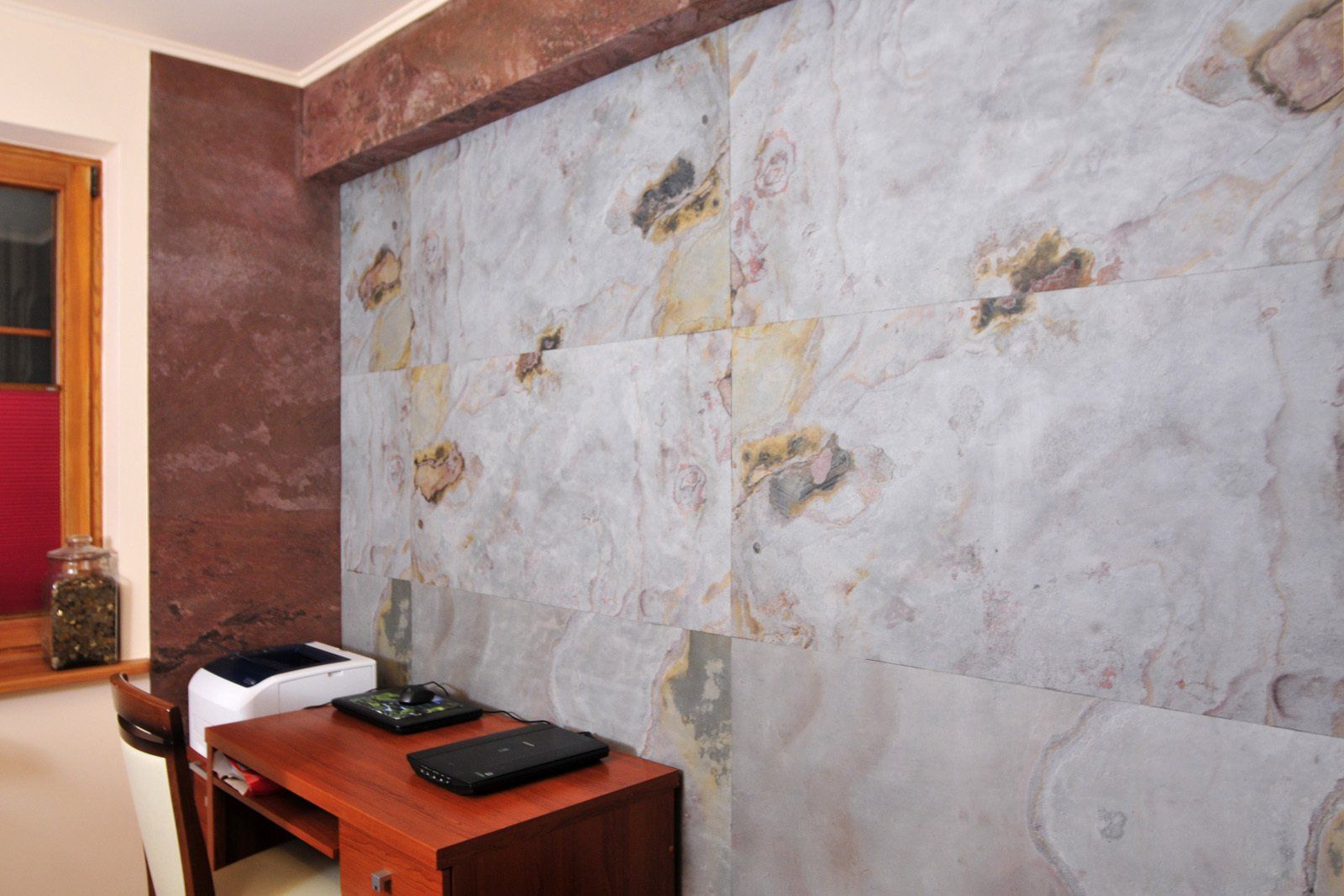 Office with wood desk, light stone wall, and dark red textured wall. Window with red shade to the left.