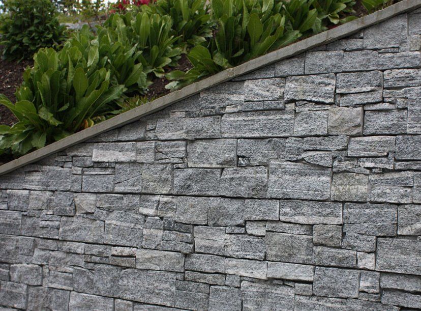 Gray stone retaining wall with green plants on top.