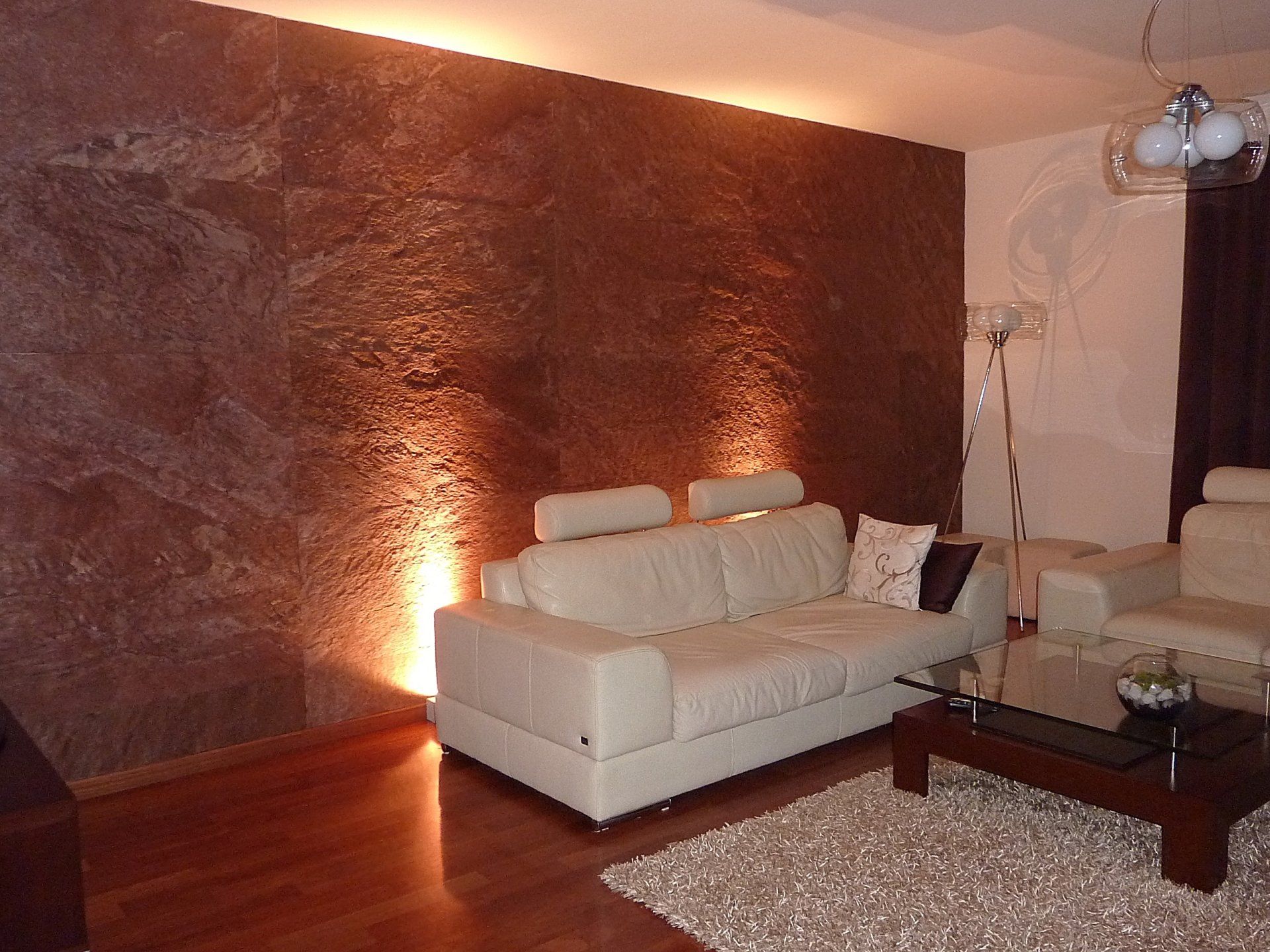 Living room with brown textured wall, off-white sofa, hardwood floor, area rug, and modern lighting.