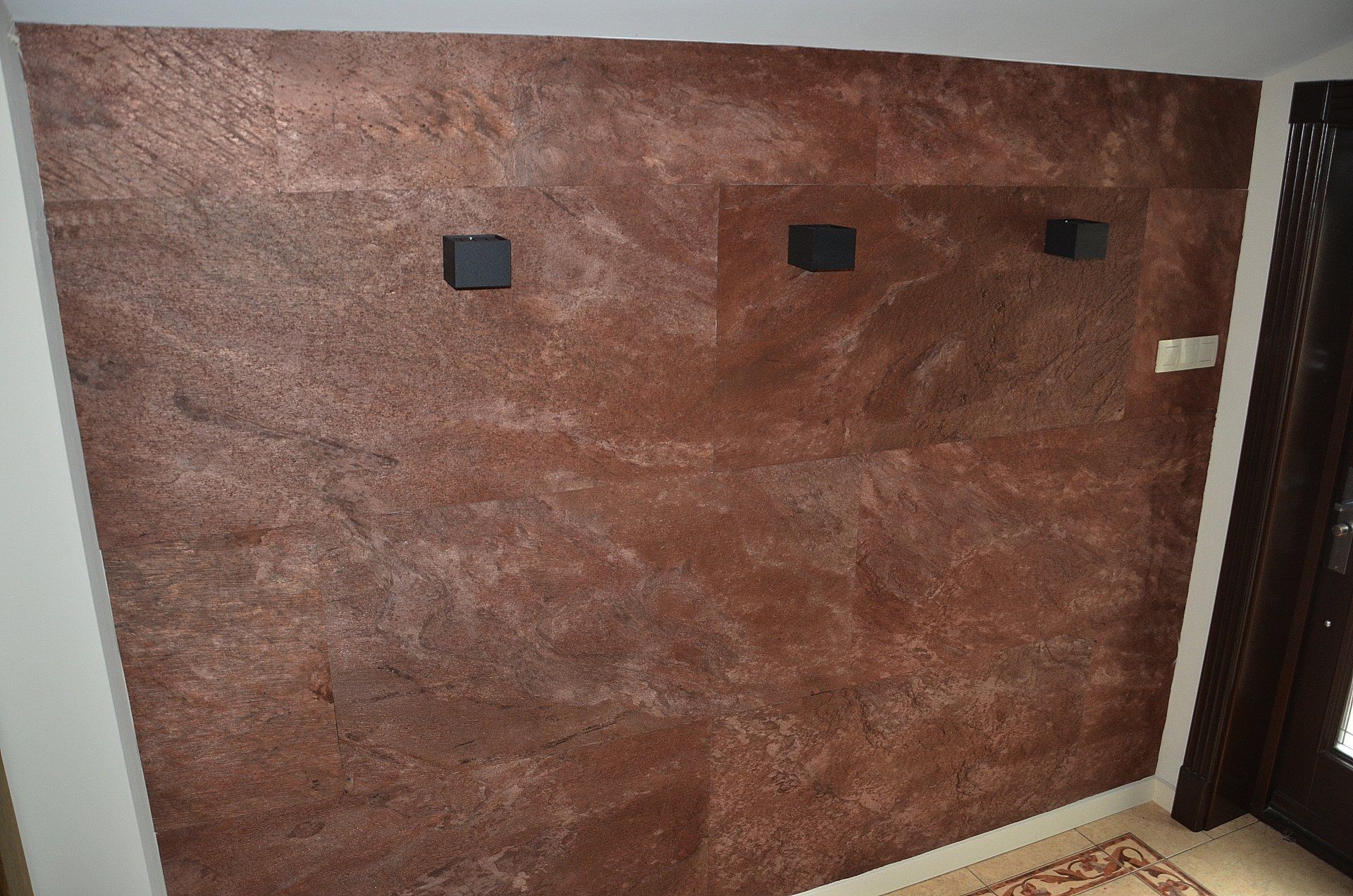 Brown textured wall with three black square lights, next to a brown door.
