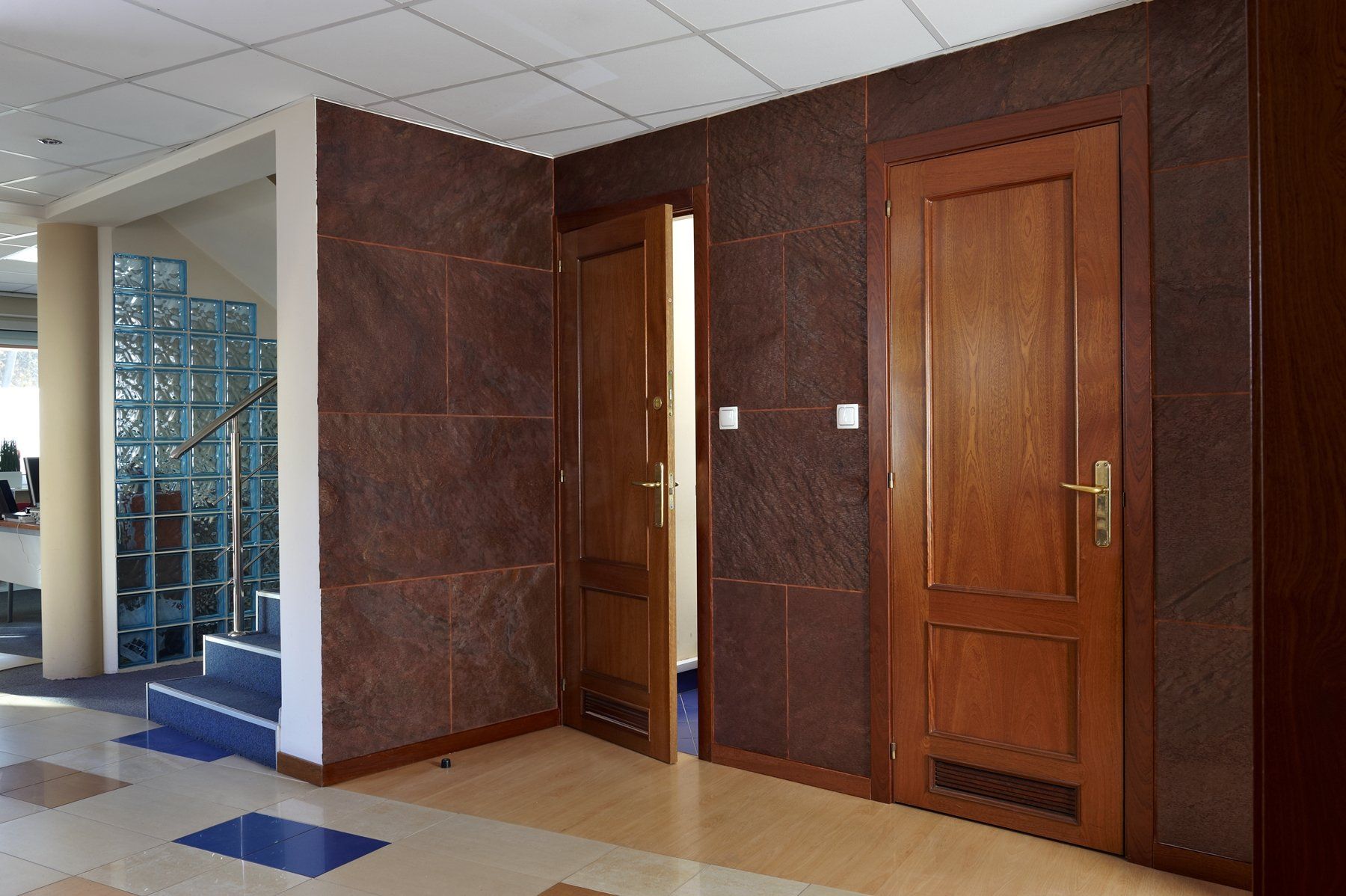 Interior hallway with brown paneled walls, wooden doors, and a staircase with glass block.