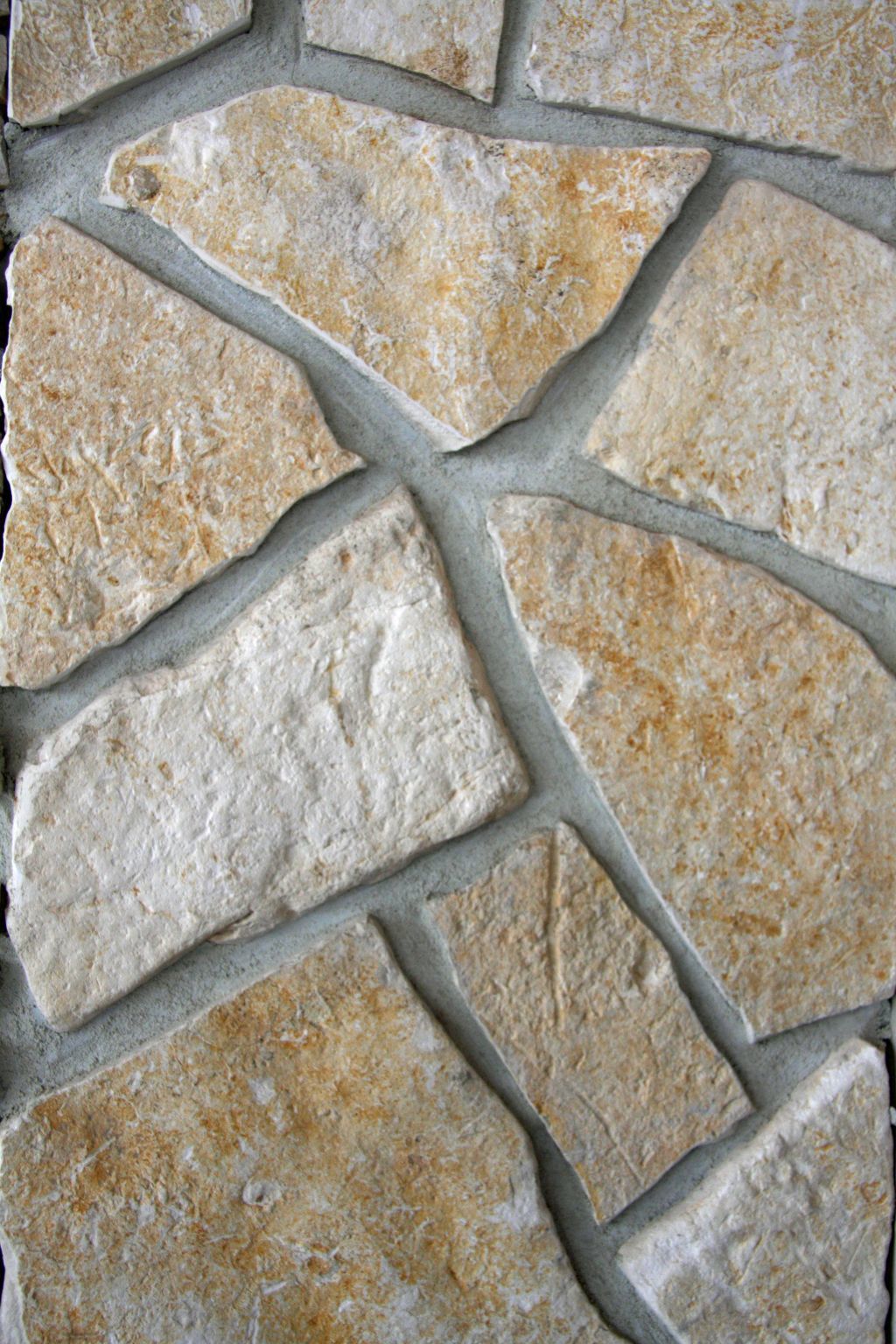 Tan and cream-colored stone tile wall with irregular, geometric shapes set in gray grout.