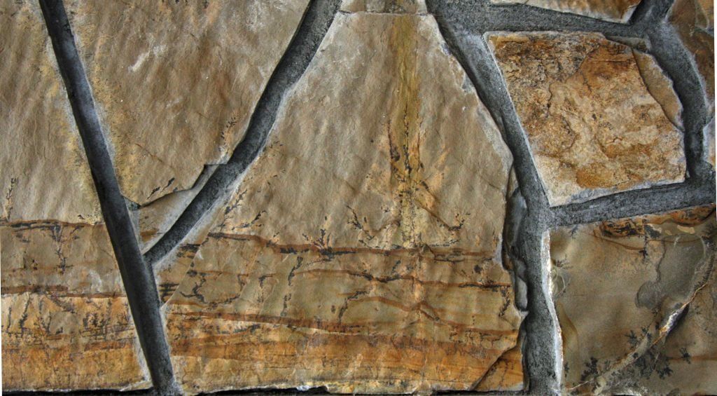 Close-up of beige and brown stone wall with dark gray grout lines.
