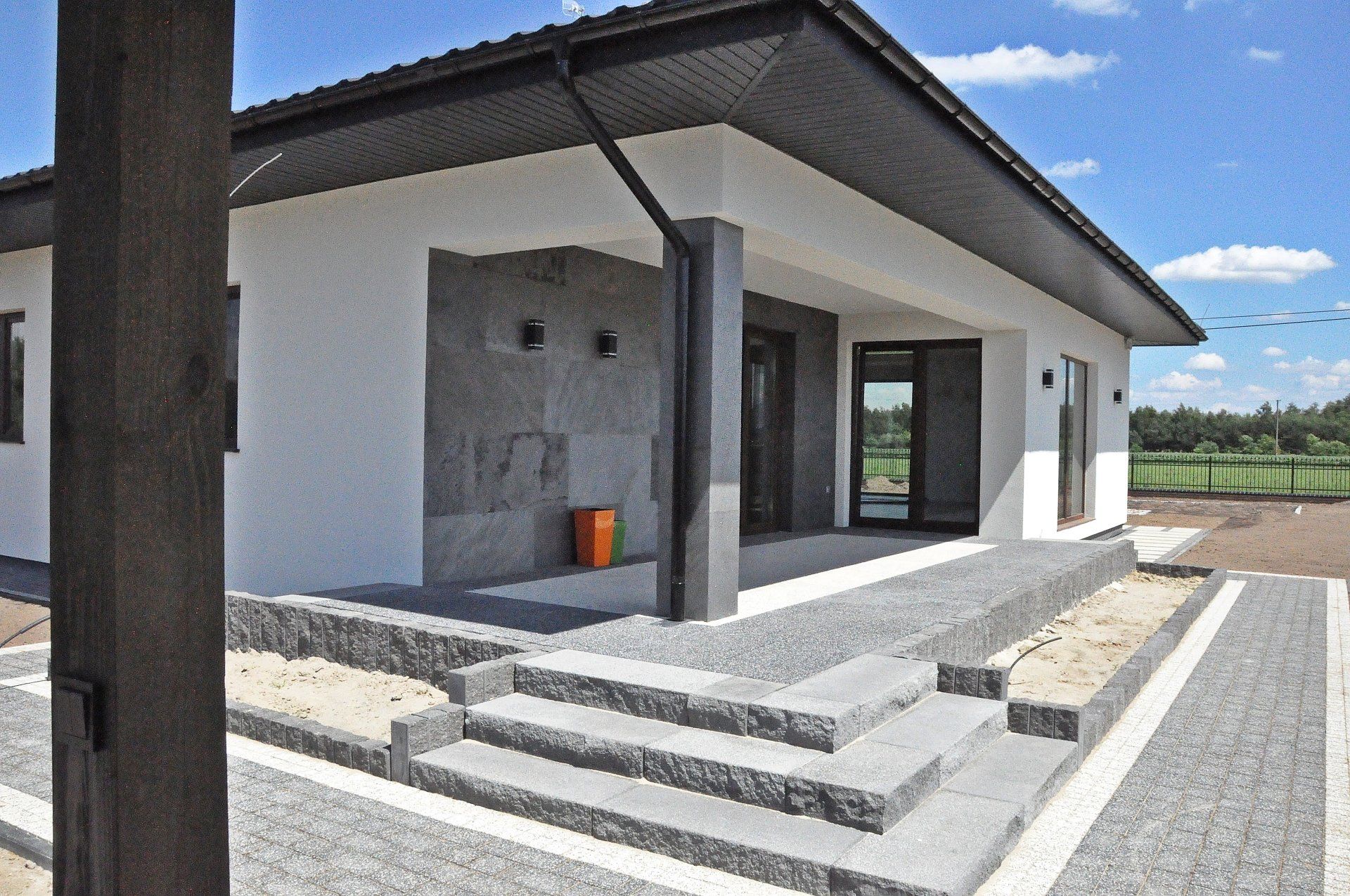 Modern white house with gray accents, steps, and a paved entrance on a sunny day.
