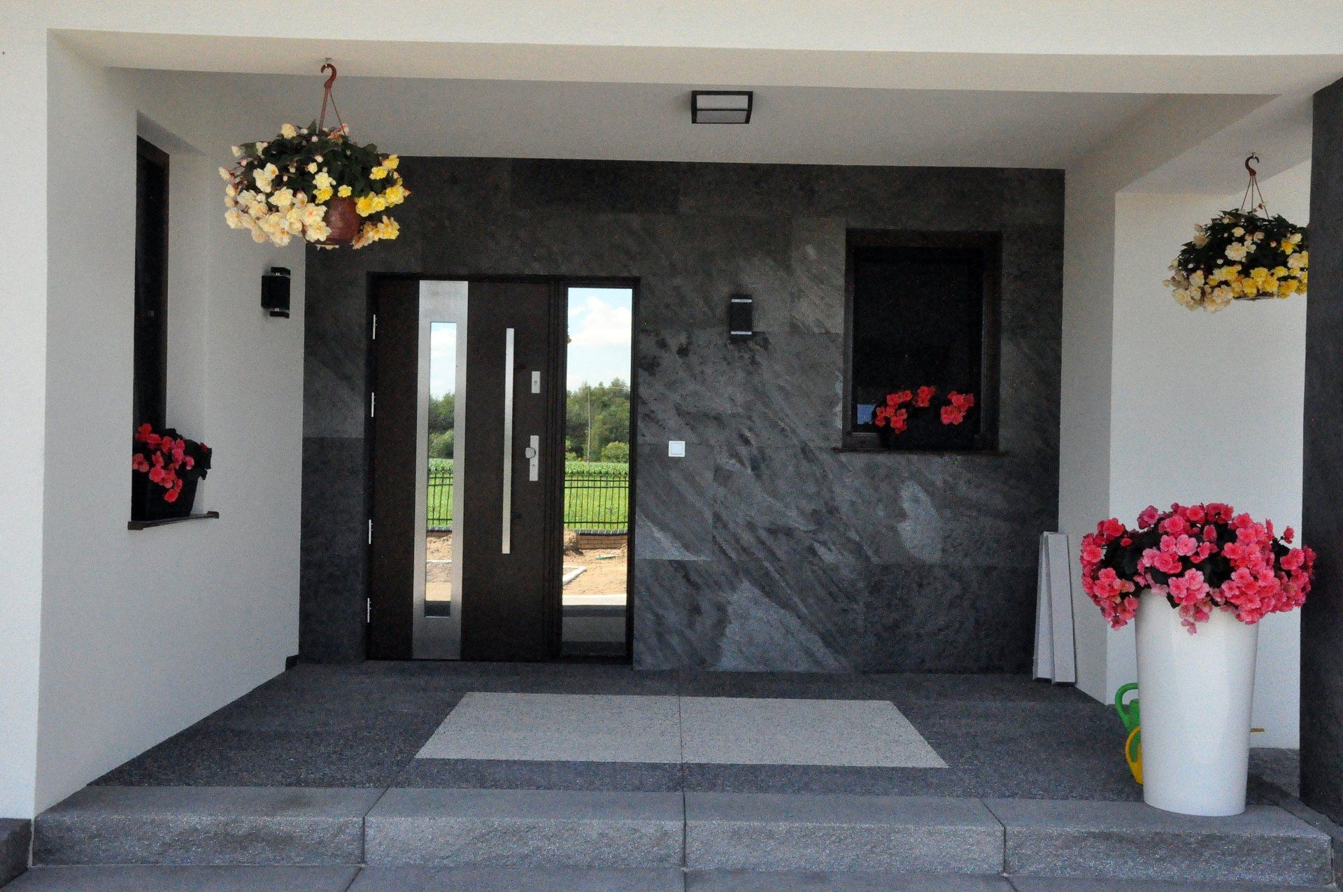 Entrance with a dark door, gray stone wall, hanging flowers, and potted flowers.
