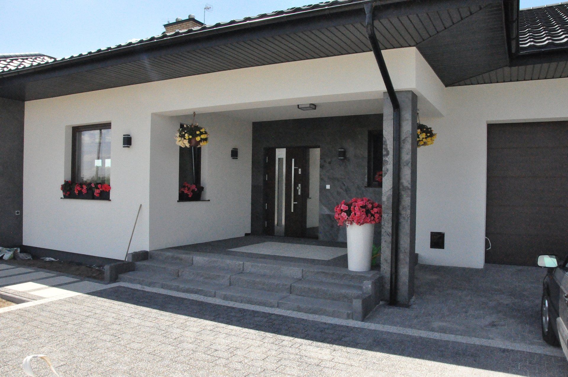 Modern house exterior with gray steps, black door, and white walls, with flowers and gray garage door.