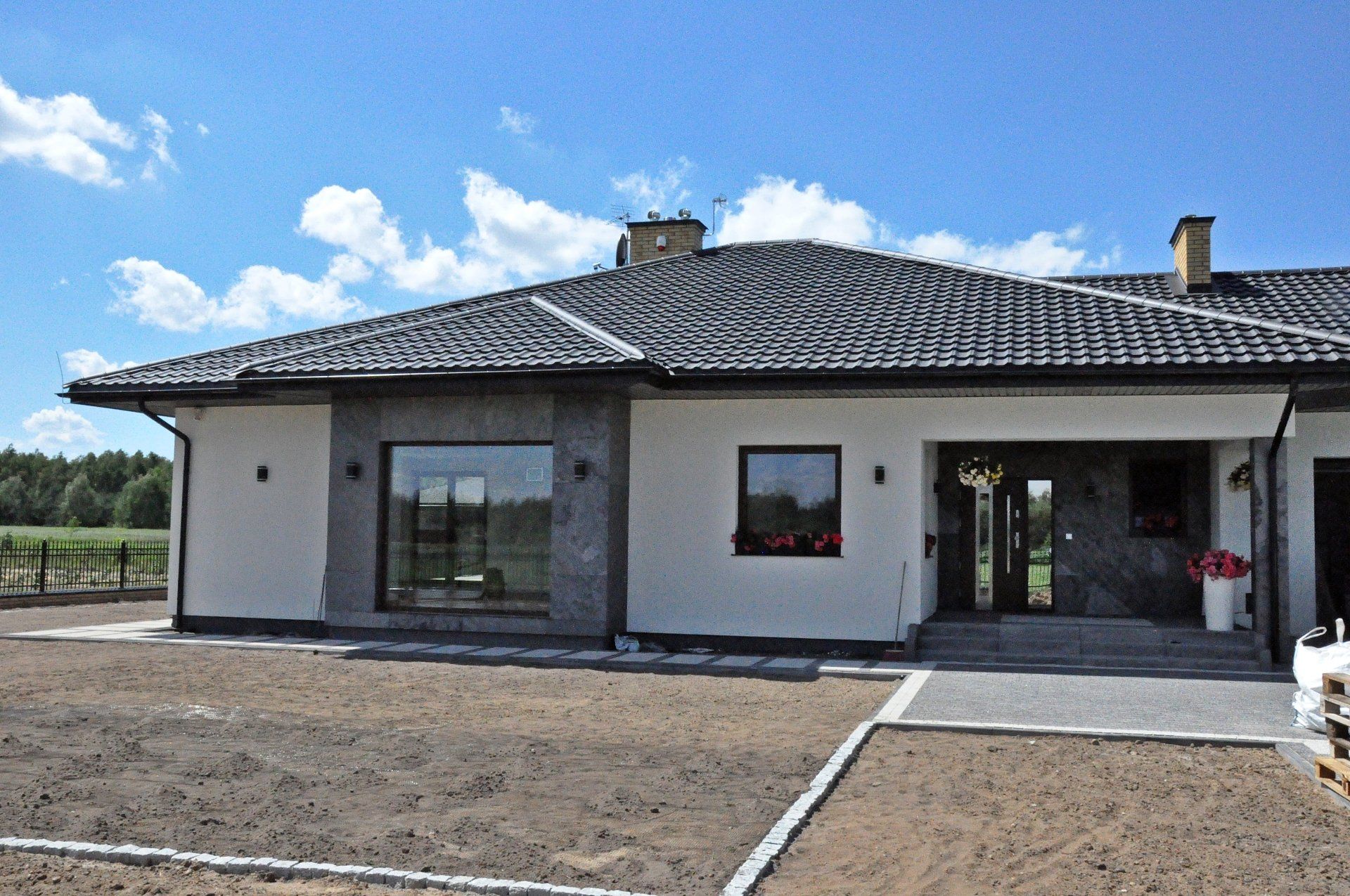 Modern one-story house with gray roof, windows, and stone accents against a blue sky.