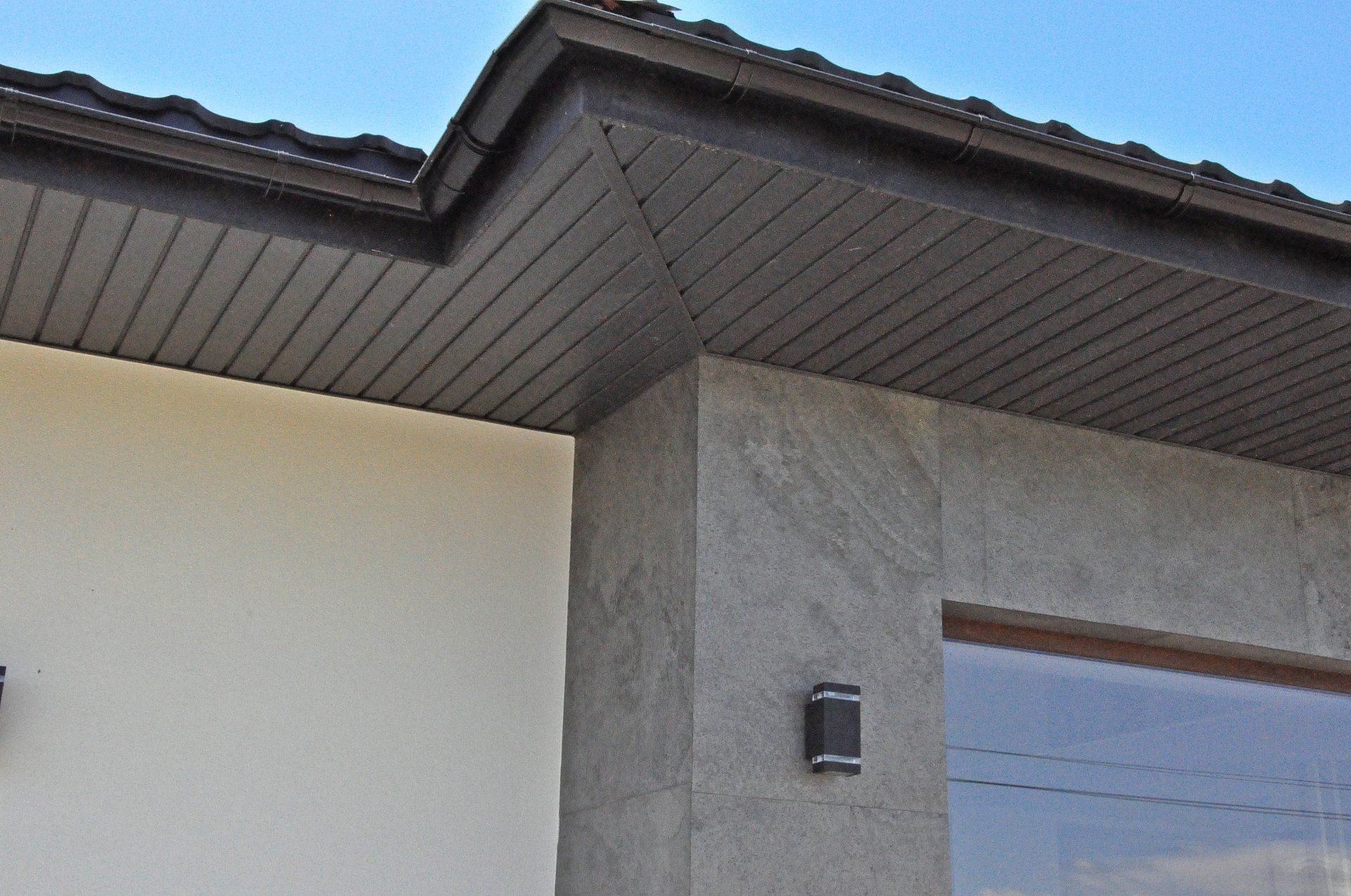 Dark brown roof overhang with gray textured wall and off-white exterior.