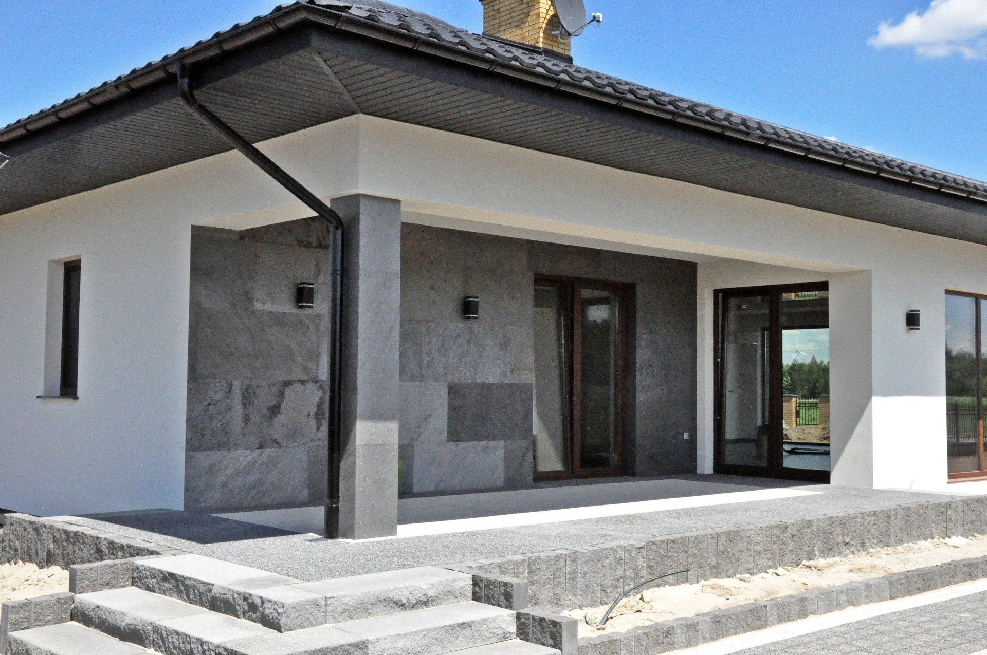 Modern bungalow with gray stone facade, white walls, and a small porch with stairs.