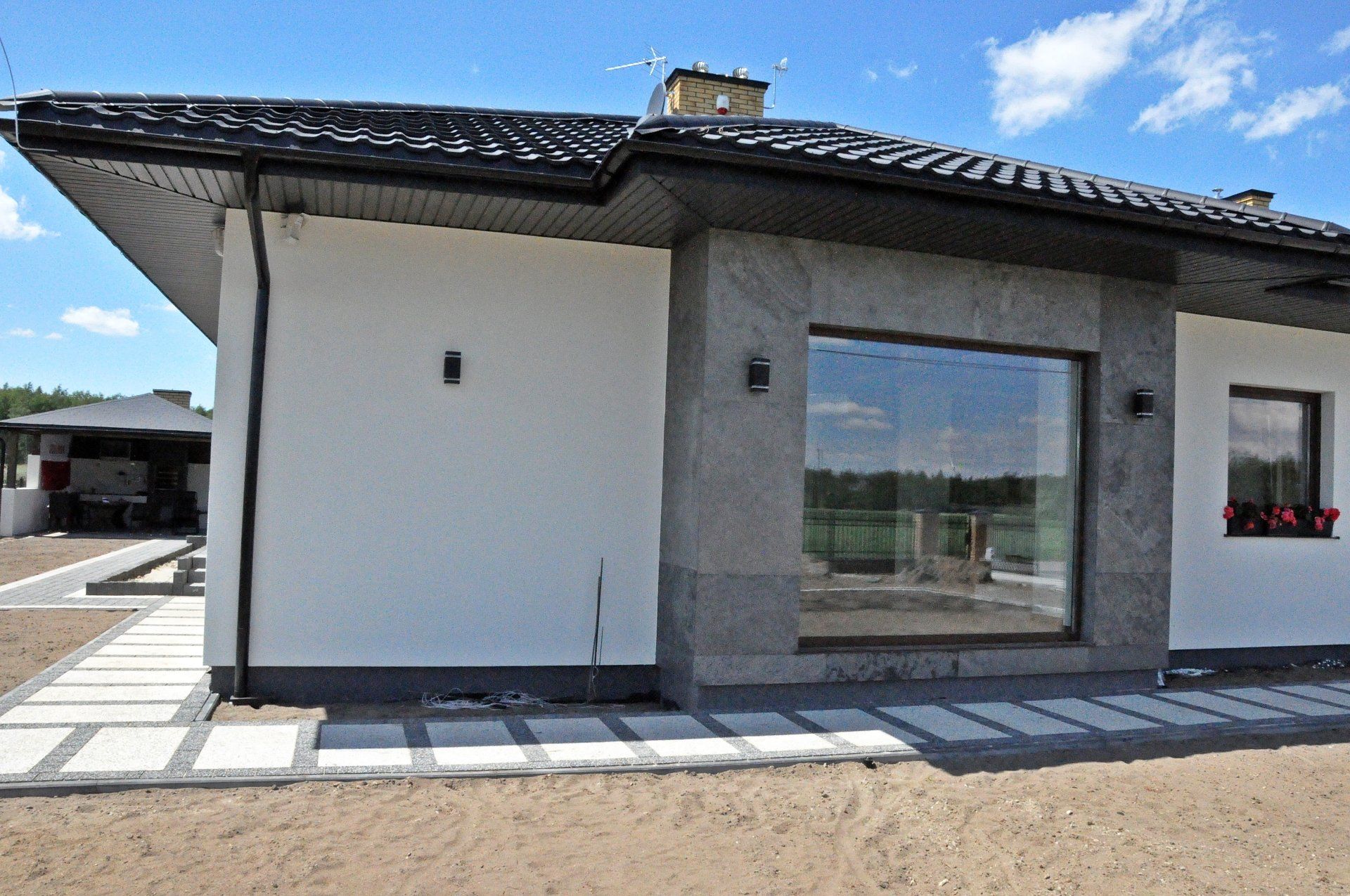 Modern home with white walls, black roof, and large gray stone window frame. Blue sky.