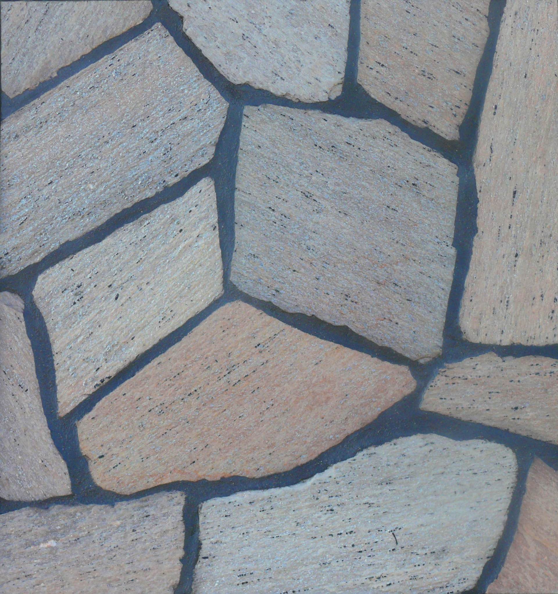 Close-up of irregularly shaped stone tiles with dark gray grout. Tiles vary in color from beige to gray.