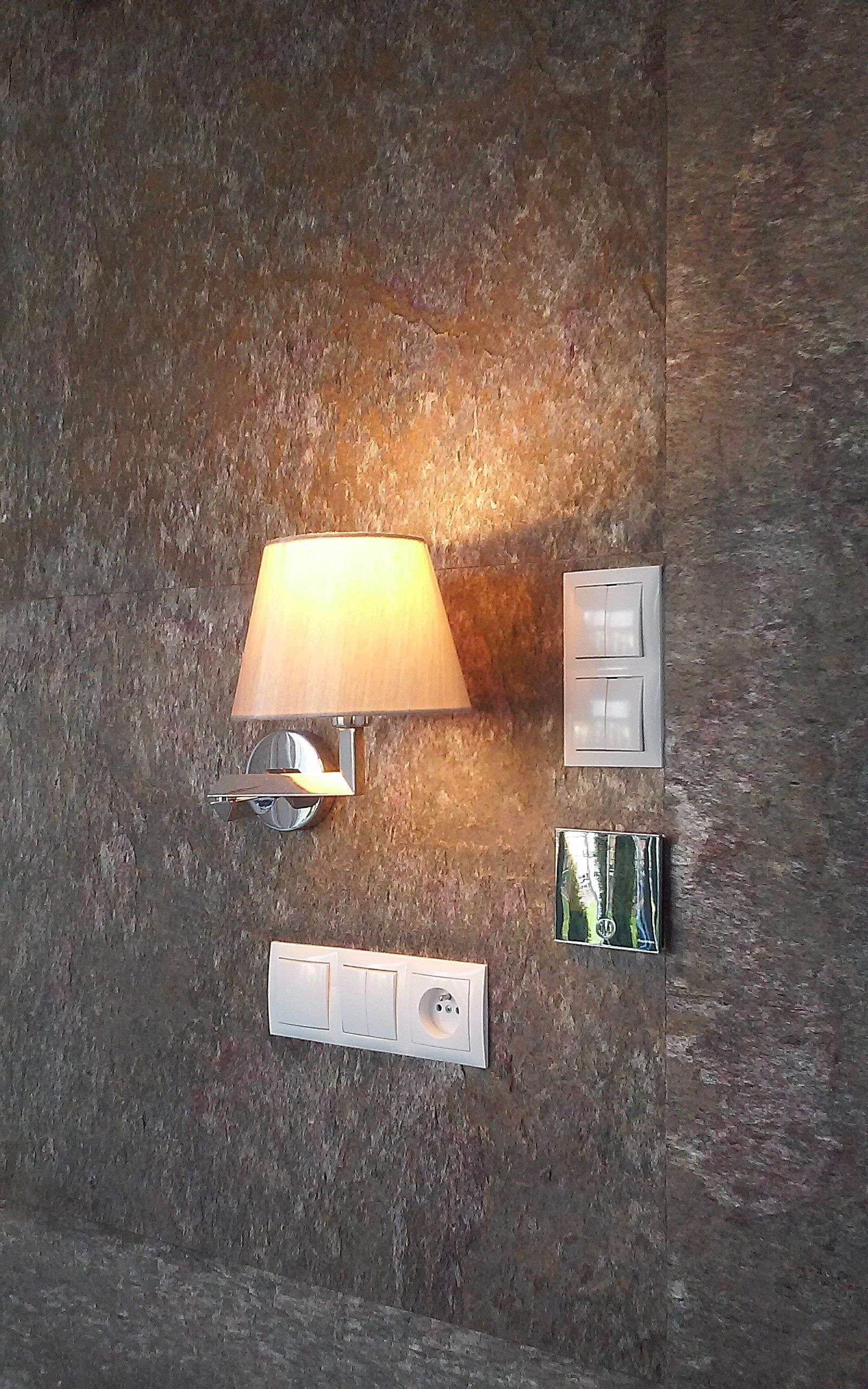 Wall with lamp, light switches, and electrical outlets against a textured brown surface.