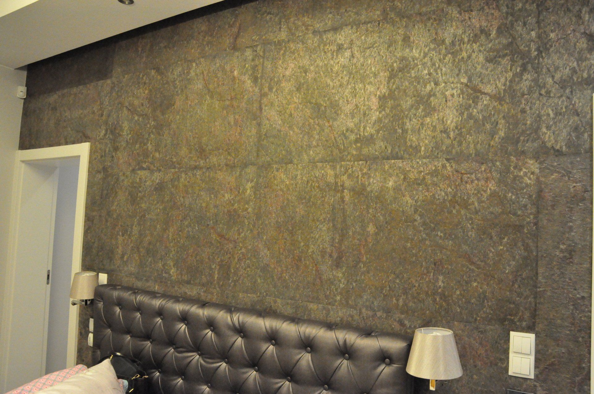 Bedroom wall with textured dark panels above a tufted headboard and lamps.