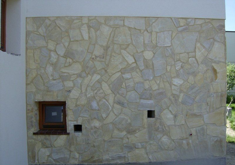 Exterior wall with light stone cladding, small window, two square openings, and a white upper section.