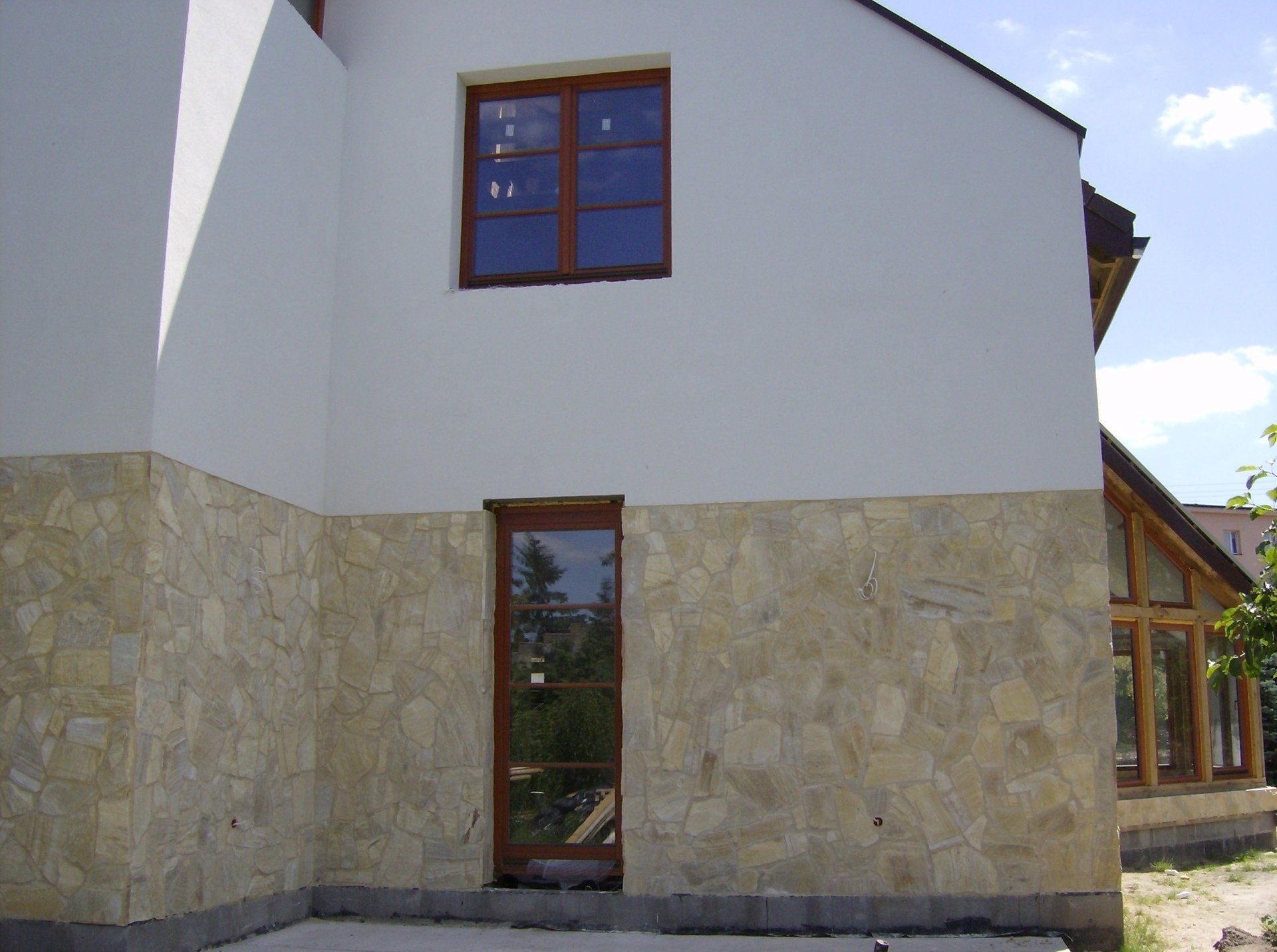 Exterior view of a building with stone cladding on the lower part and white stucco above, with a door and window.