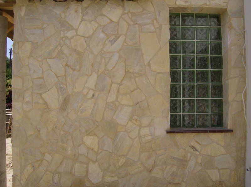 Exterior wall with light-colored stone facade and a rectangular window with green-tinted glass blocks.