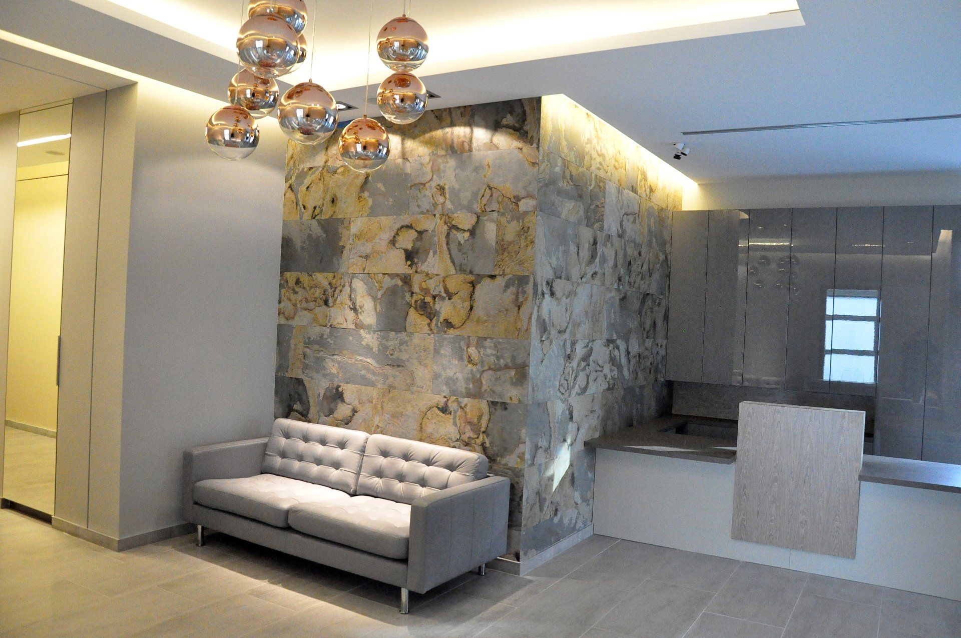 Lobby with gray sofa, stone wall, modern light fixture, and reception desk.