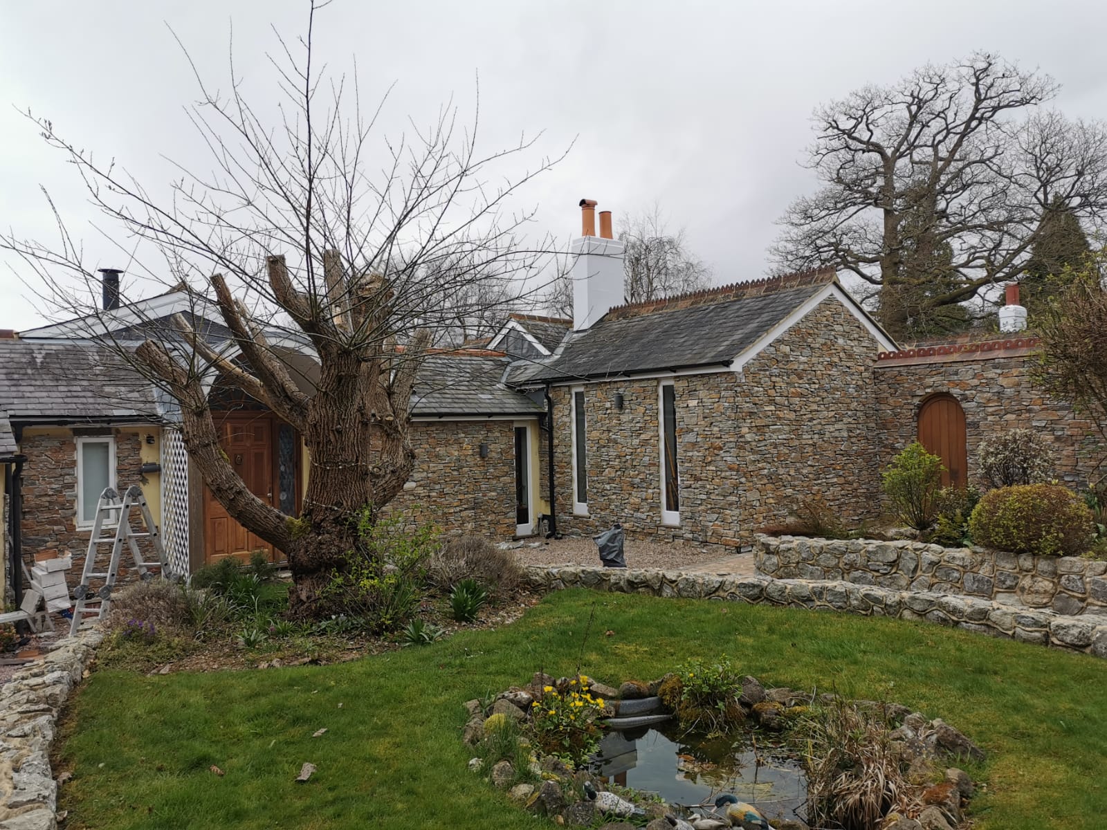 Stone cottage with small pond in a garden on a cloudy day.