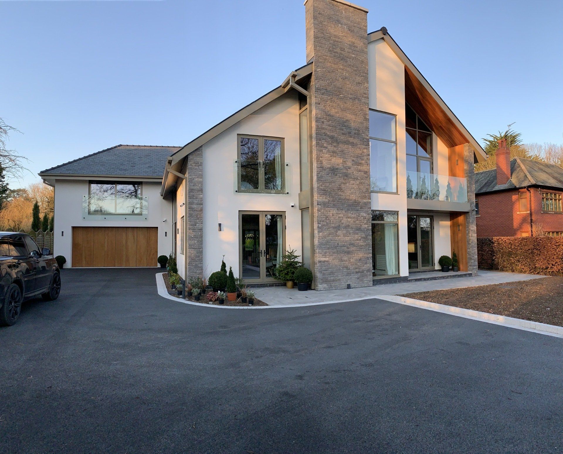 Modern house with white walls, stone accents, large windows, and a driveway.