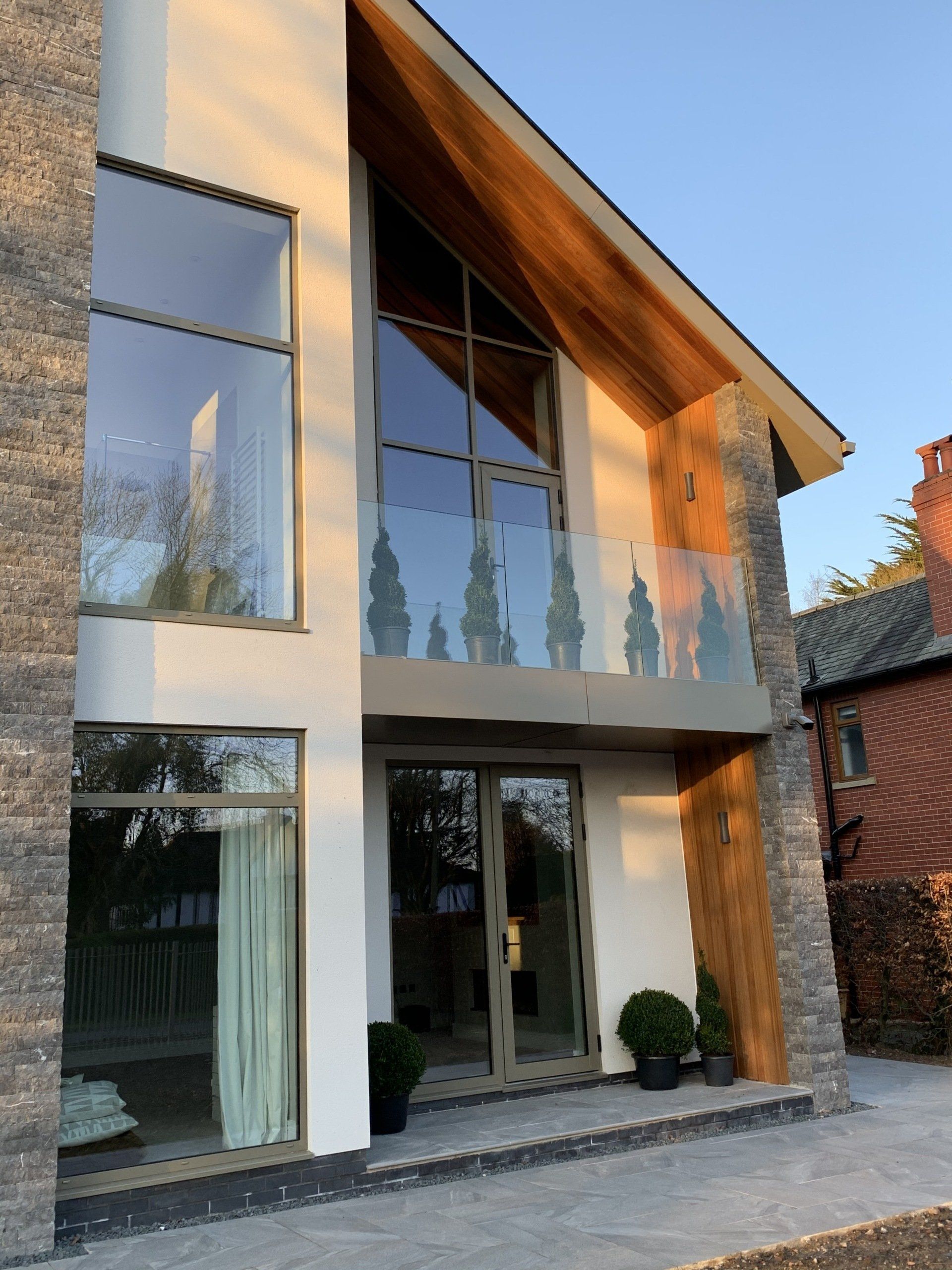 Modern house with large windows, stone accents, and wooden roof.