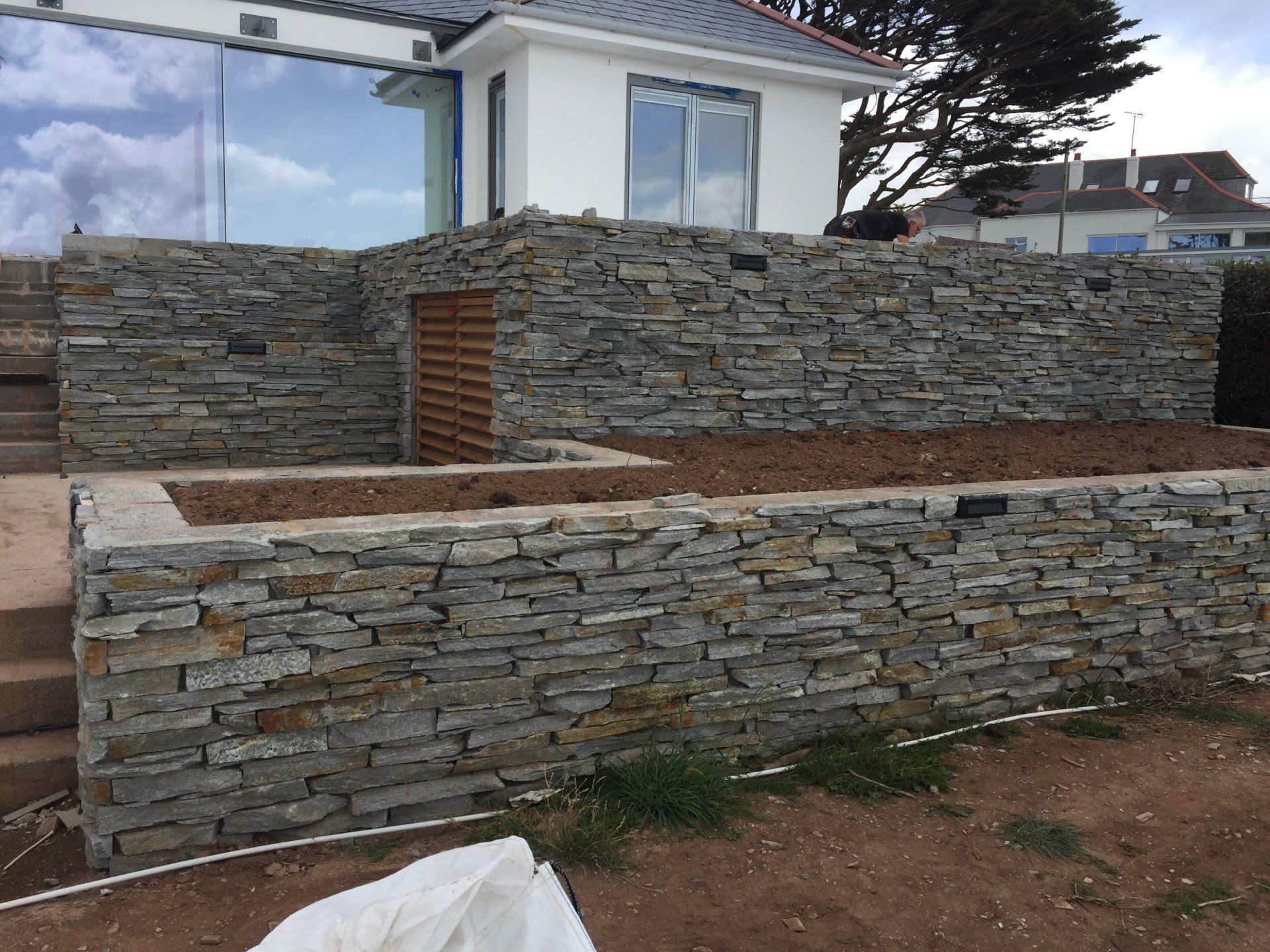 Stone retaining walls with steps and raised garden beds in front of a white house.