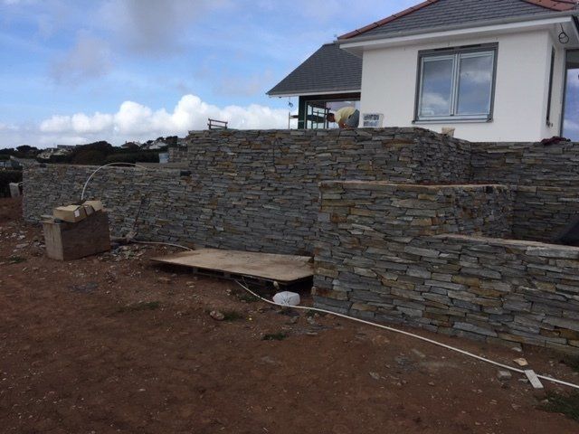 Stone retaining walls constructed on a hillside next to a white house with a red roof.
