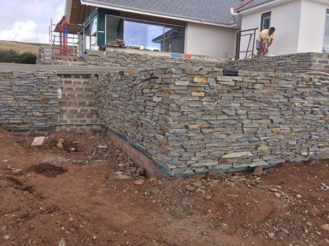 Stone retaining walls being built in front of a house, construction in progress.
