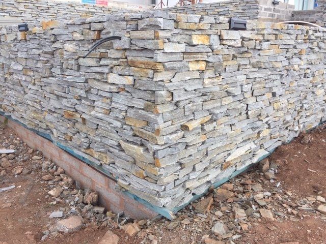 Stone veneer construction on a building foundation corner, showing layered gray and tan stones.