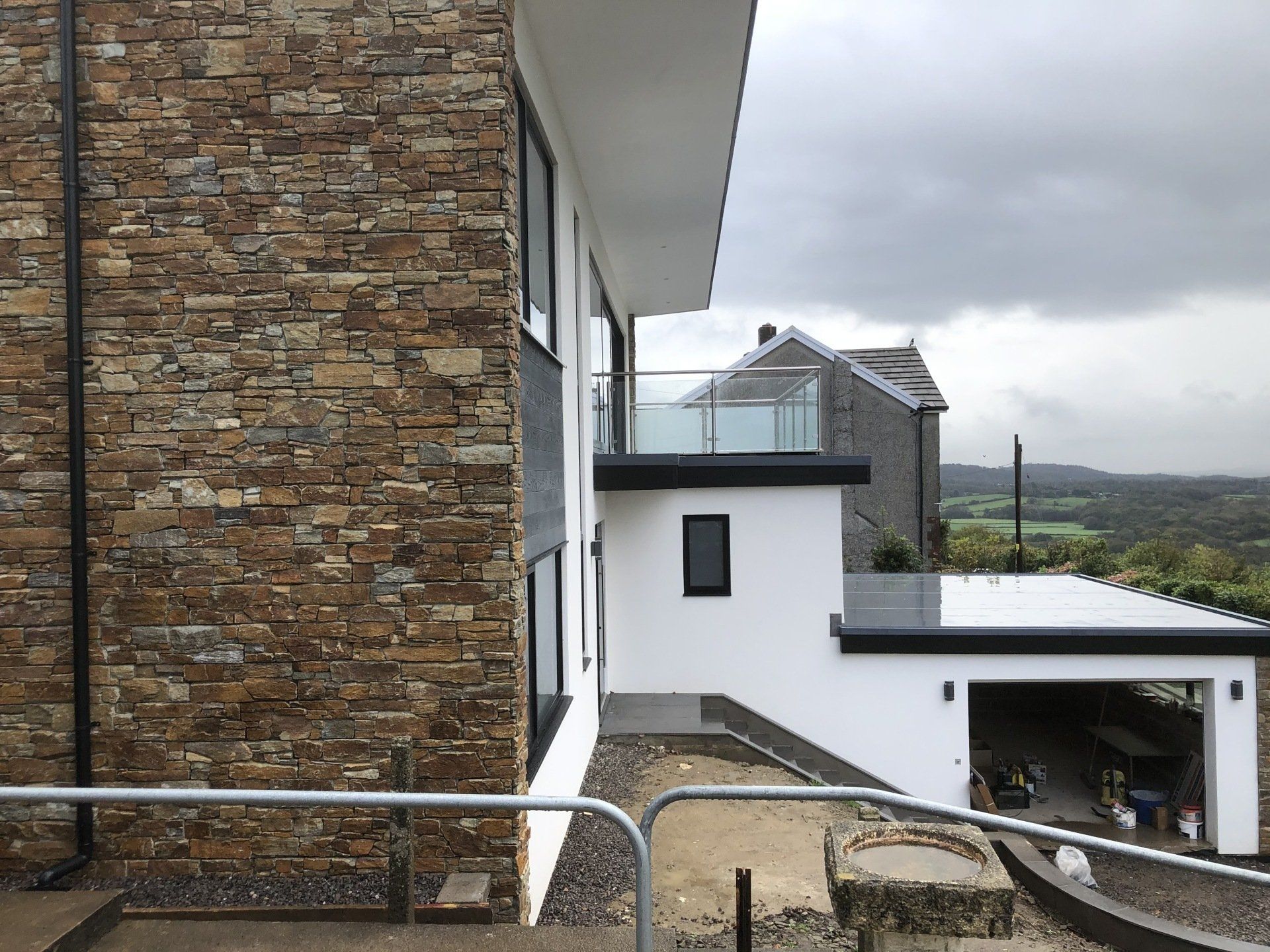 Modern house with stone and white facade; balcony with glass railing; overcast sky.