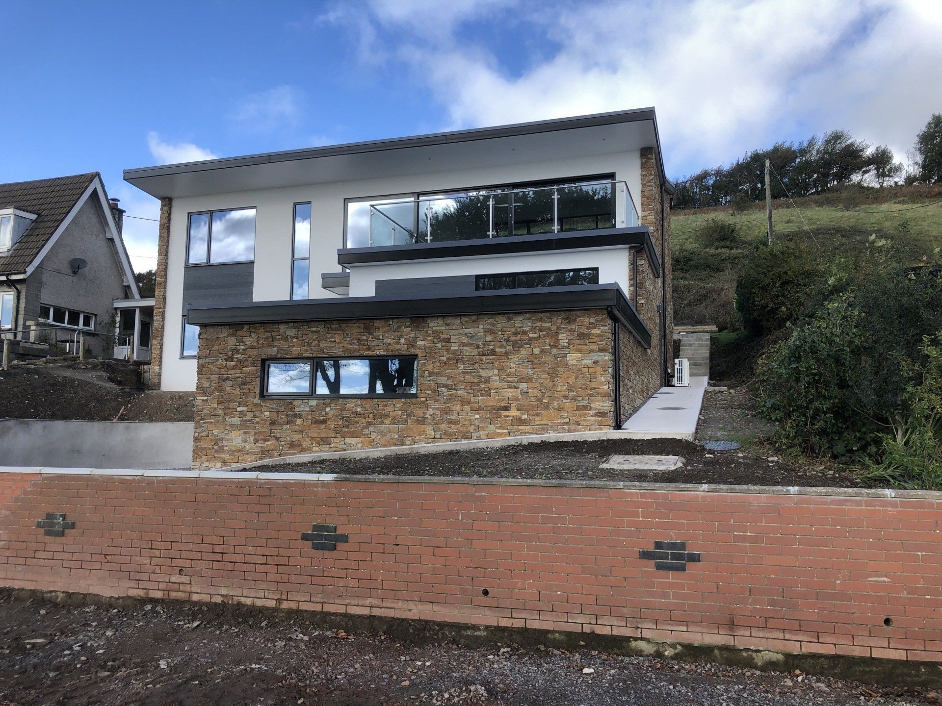 Modern two-story house with stone facade, large windows, and flat roof. Situated on a sloped lot.